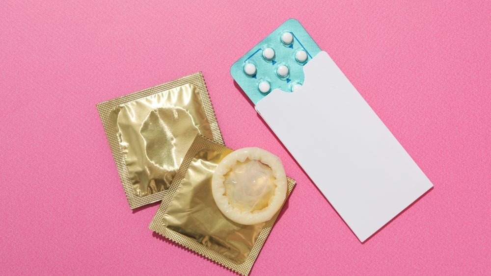 Condoms and birth control pills on a pink background, place for text