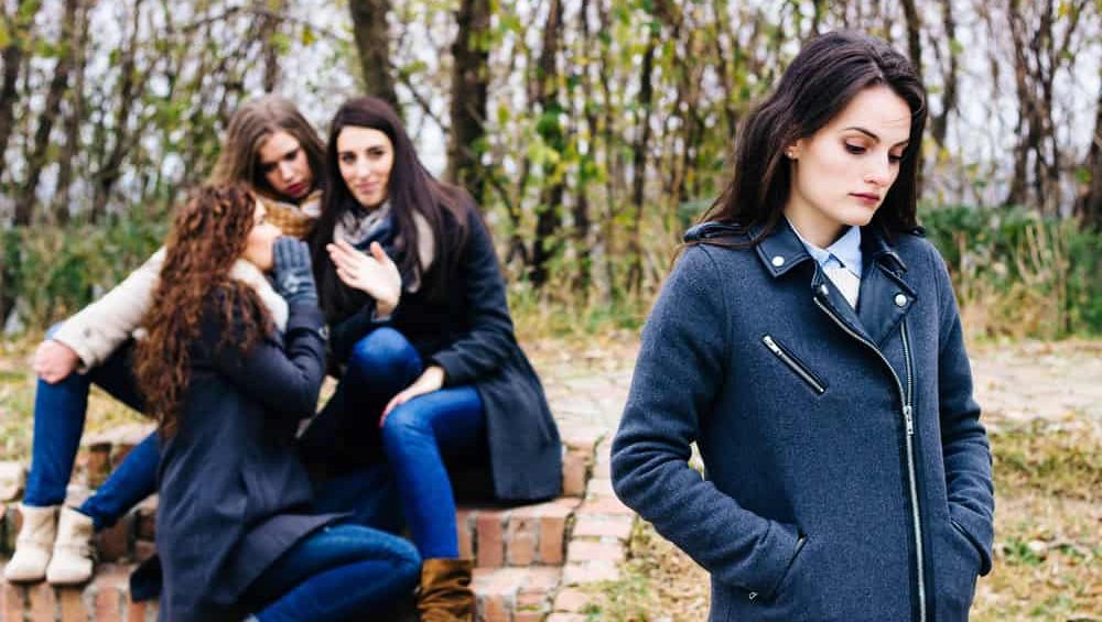Sad girl with friends gossiping in background, behind her back