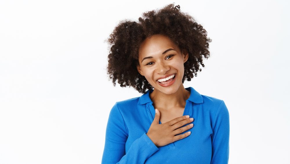 Portrait of young woman, express gratitude, says thank you, holds hand on chest and smiles, appreciation gesture, white background.