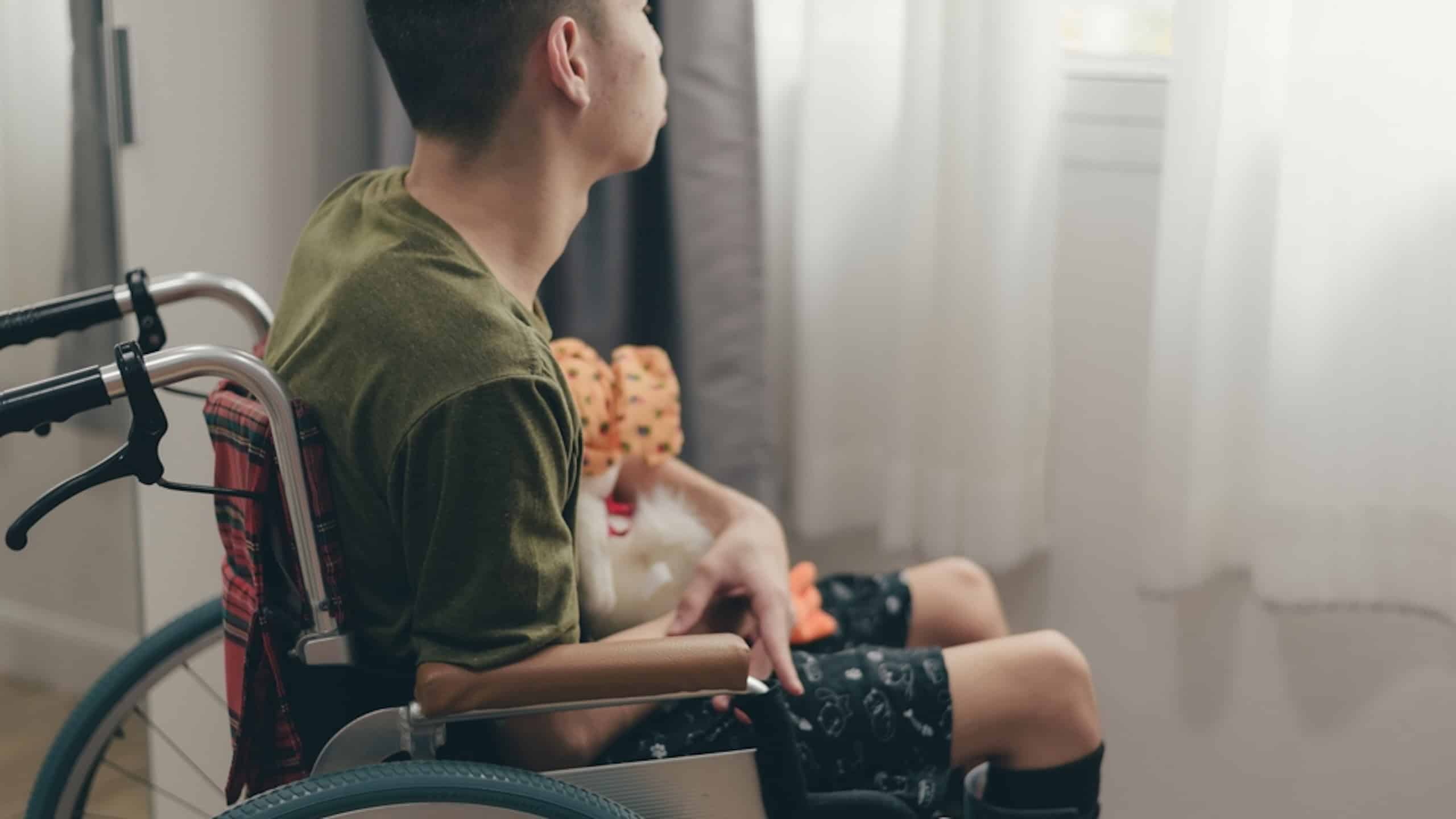 Young man with disability on wheelchair hug doll in the bedroom lonely, Depression occurs in people with disabilities who are alone at home, World mental health day and mental rehabilitation concept.