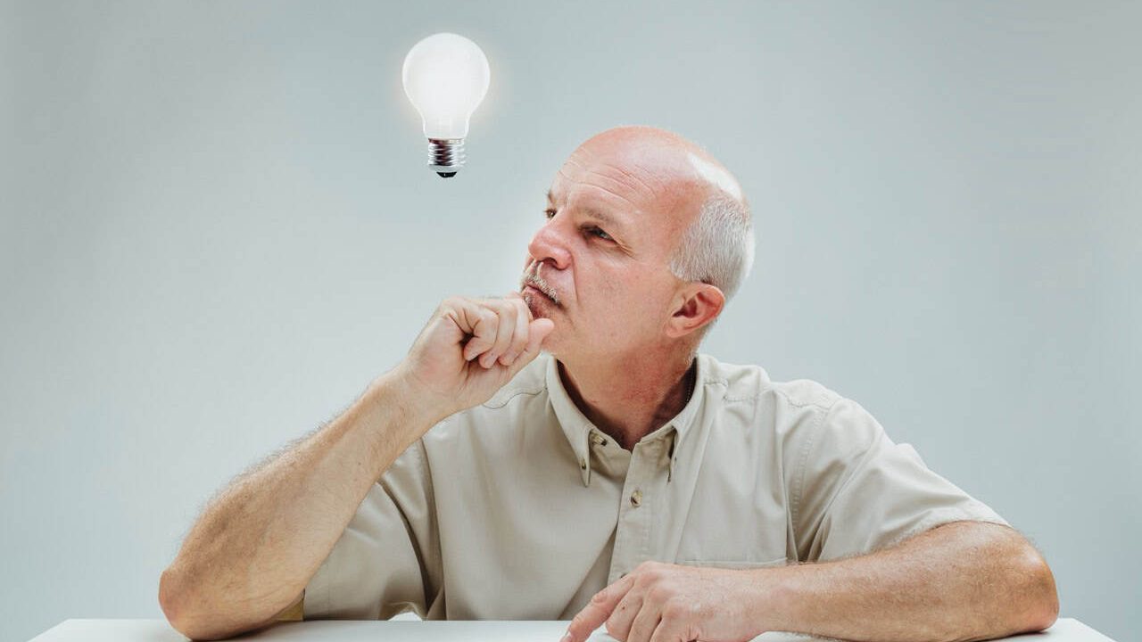Contemplative mature male gazes at the illuminated bulb overhead, signifying a moment of inspiration