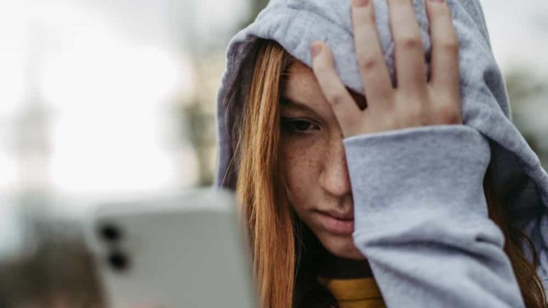 Portrait of teenage girl looking at her smartphone, sad, anxious, alone. Cyberbullying, girl is harassed, threated online.