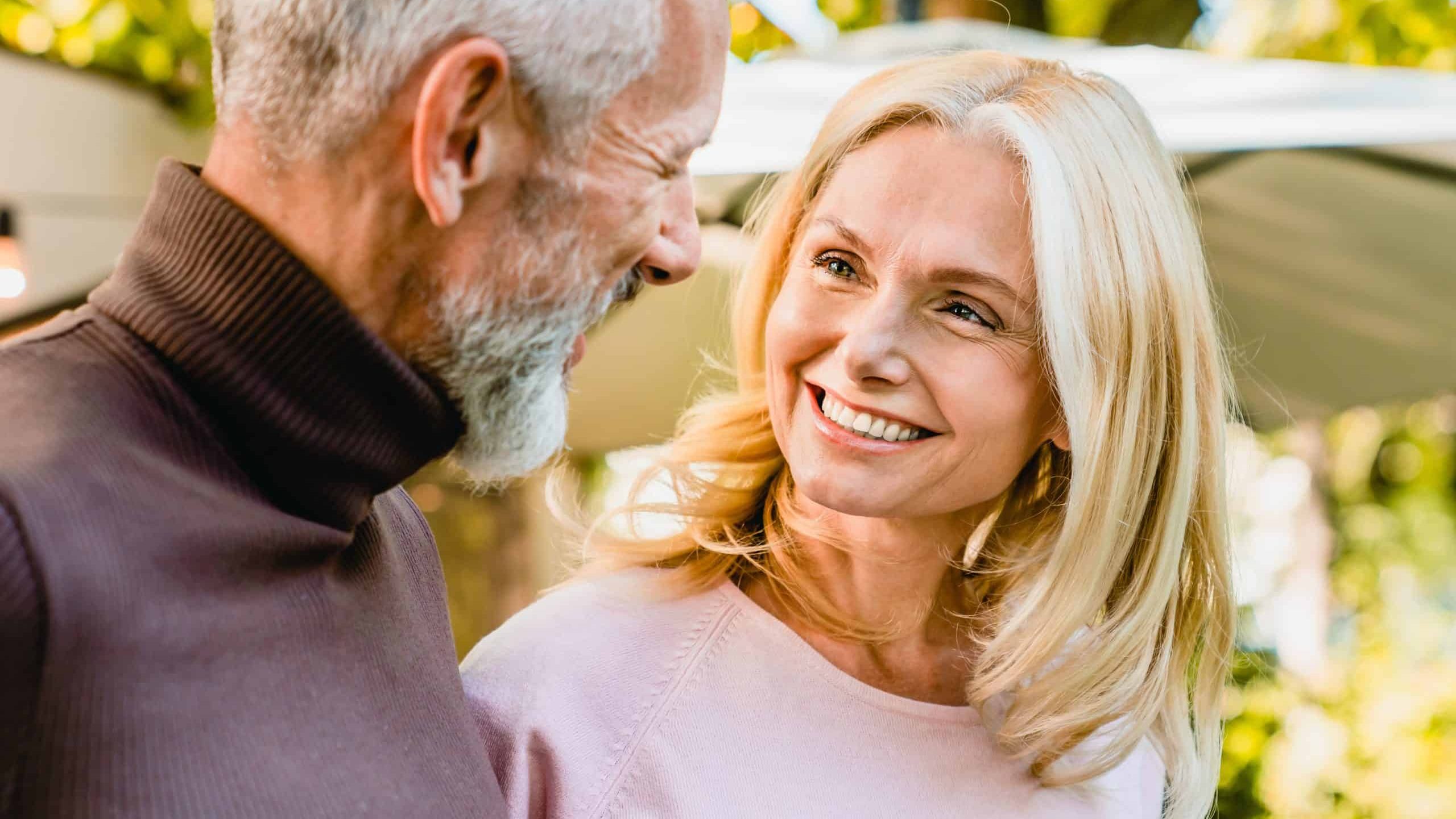 Cheerful senior couple looking at each other with passion and love in the park. Middle-aged spouses having romantic date outdoors outside. Quality time - love language