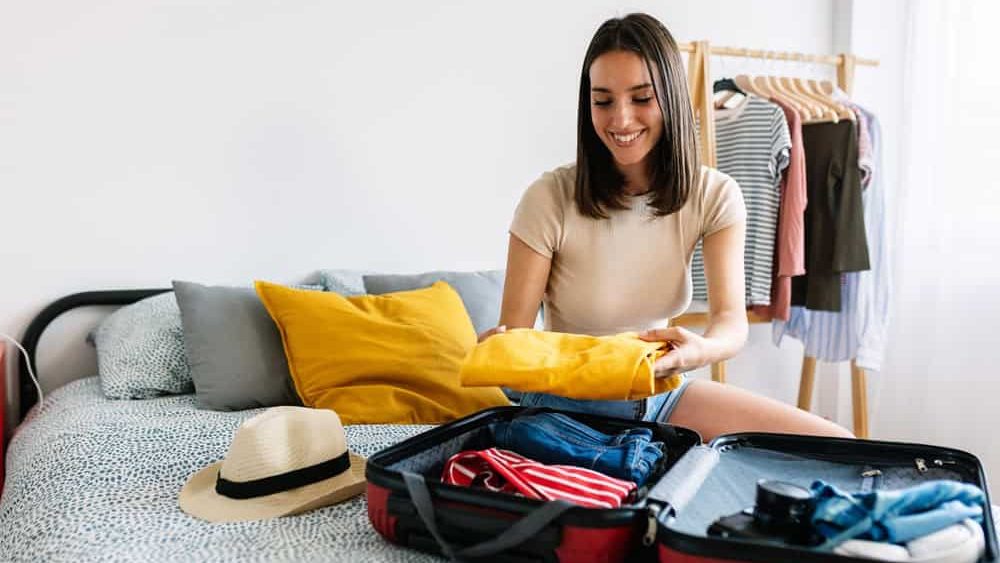 Happy young woman preparing luggage before summer travel vacation or weekend getaway. Packing preparation before holiday departure