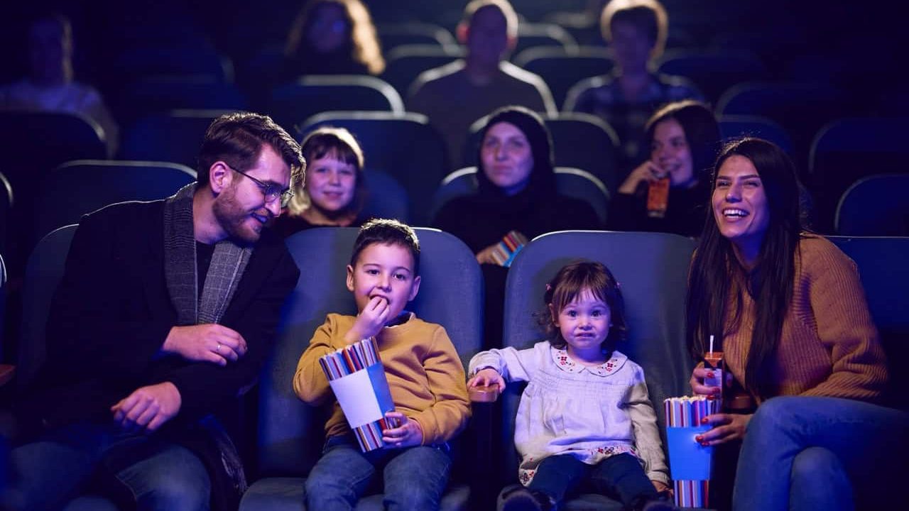 A modern family enjoys quality time together at the cinema, indulging in popcorn while watching a movie with their children