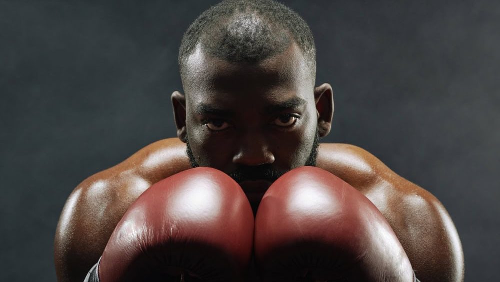 Dramatic closeup portrait of Black muscular boxer looking at camera with intense face expression over red gloves