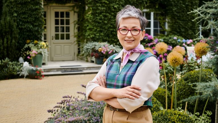 elegant mature joyous woman with short hair and glasses smiling at camera near her house in England