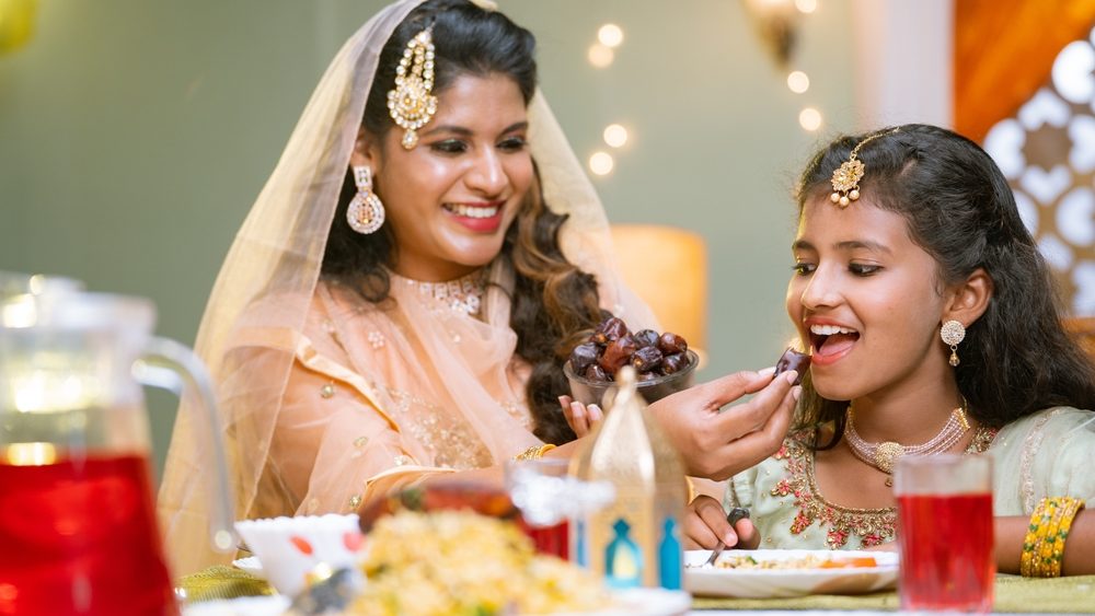 Happy indian mother feeding dates to daughter during ramadan iftar dinner at home - concept of caring mother, ramazan festival and healthy eating.