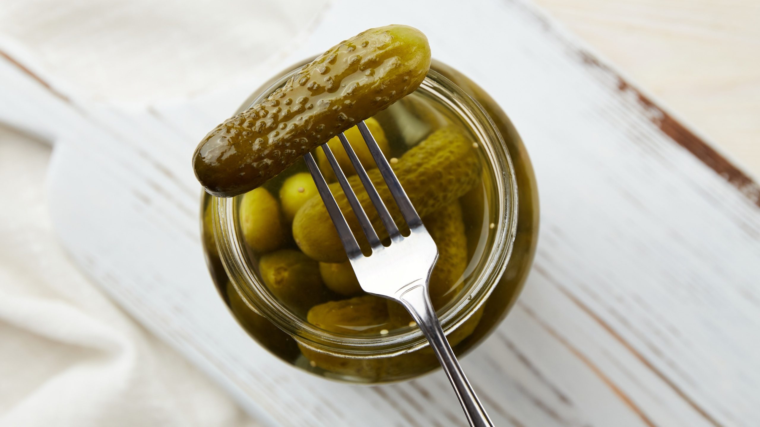 Pickled cucumbers on a fork and in a jar on a wooden background.