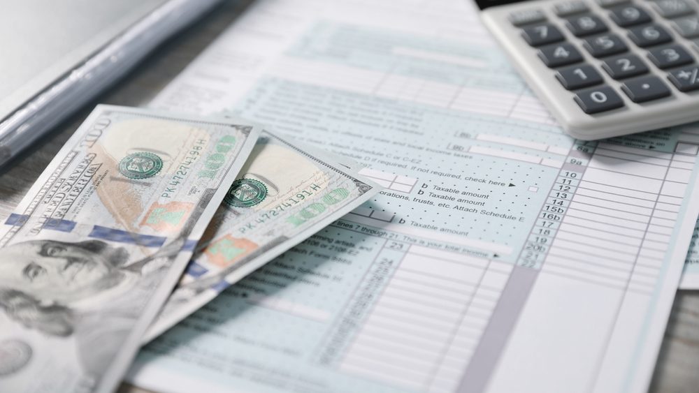 Payroll. Tax return forms, calculator and dollar banknotes on table, selective focus