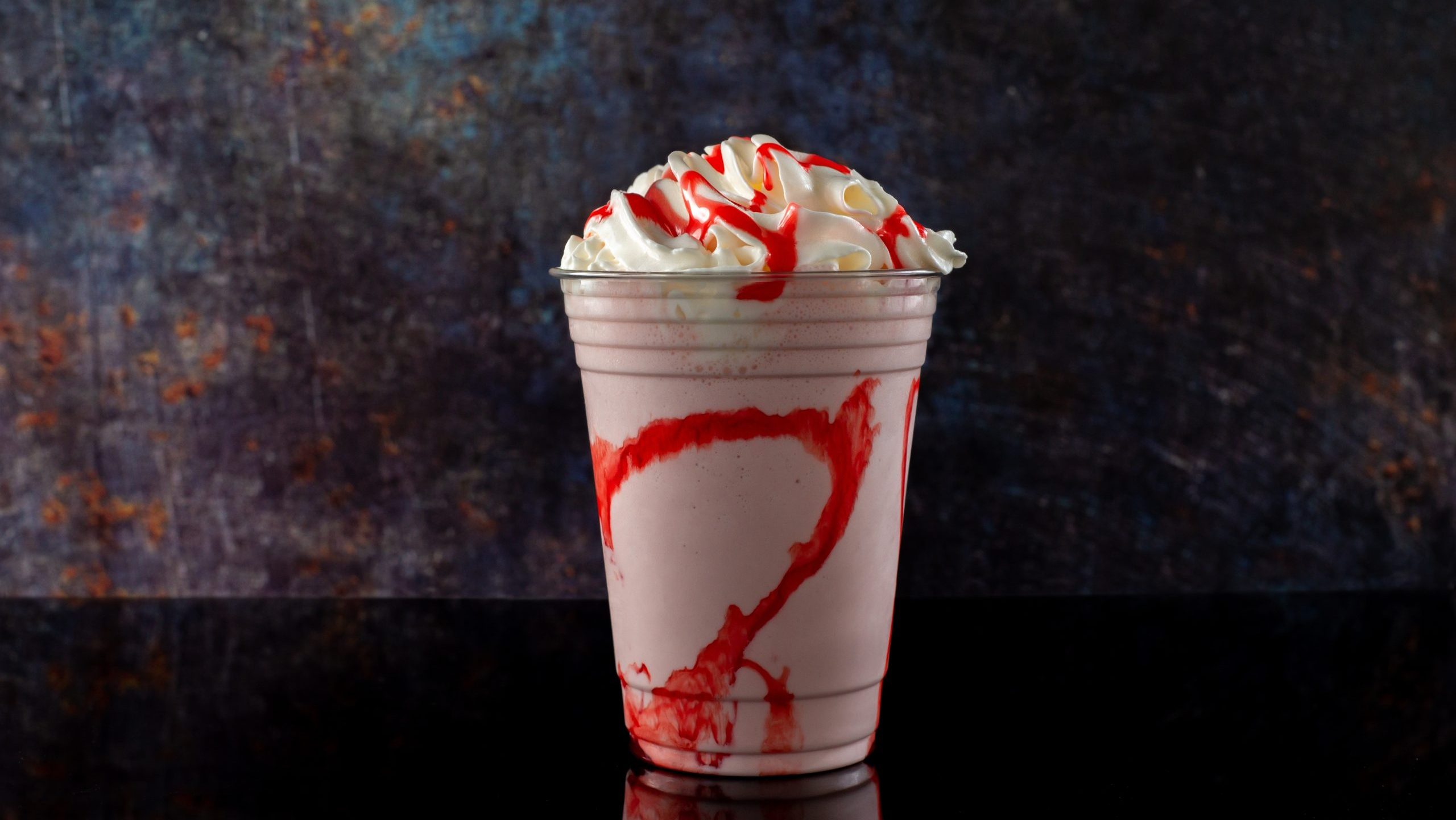Strawberry milkshake with strawberry syrup in clear glass on dark background.