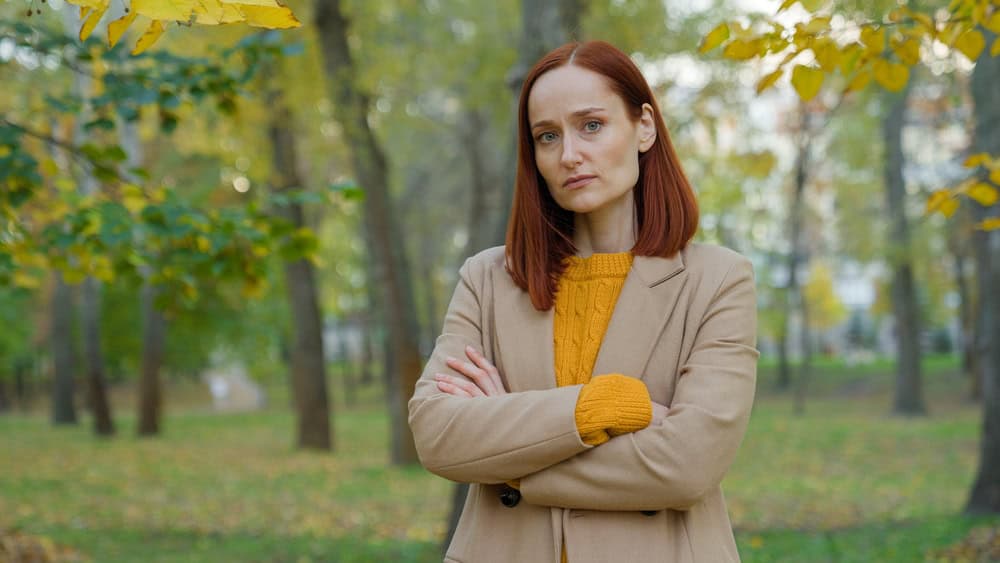 Serious offended Caucasian woman in autumn park in city outdoors posing confident alone looking at camera angry sad upset girl lady crossed hands on chest stressed female in fall season crossing arms