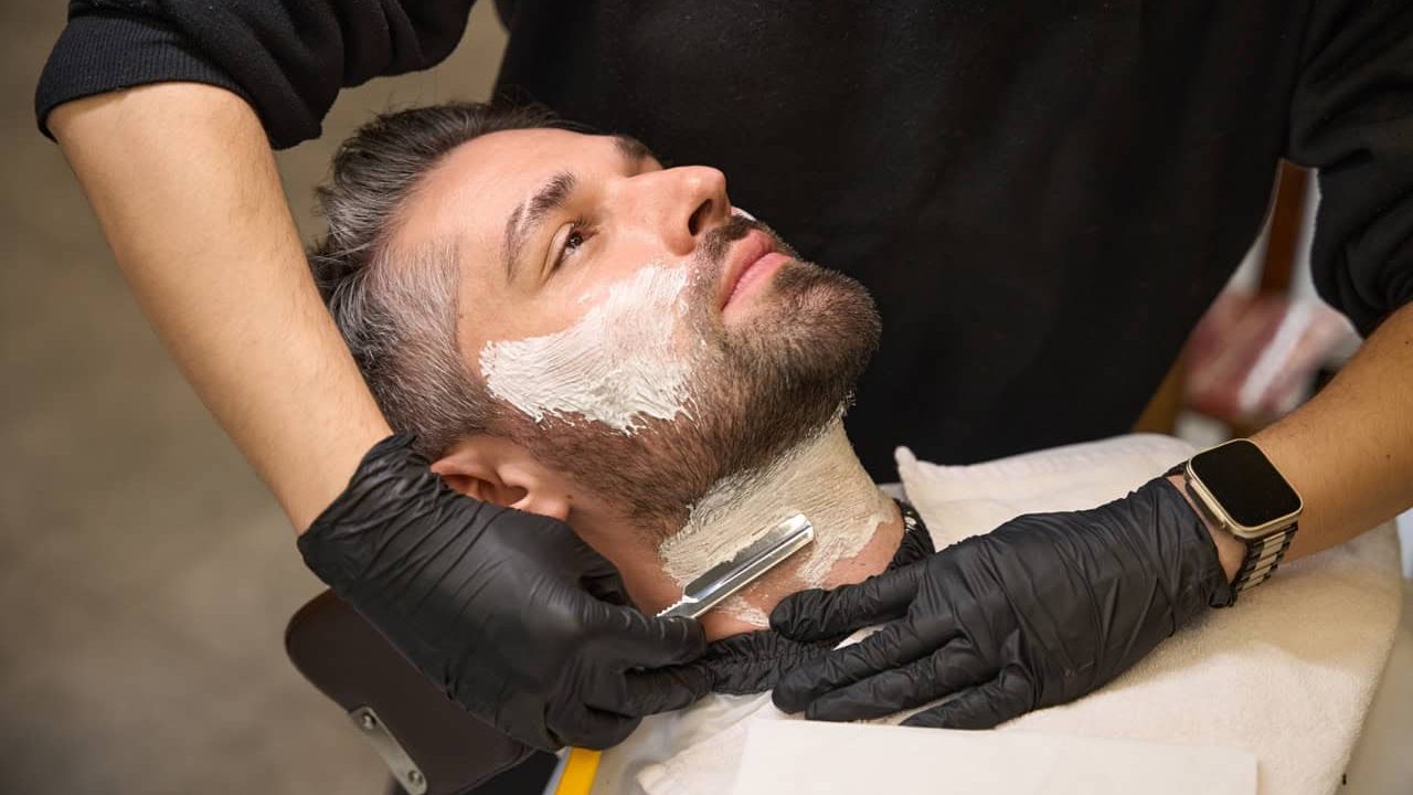 Barber applying shaving cream on client's neck and follow by straight razor