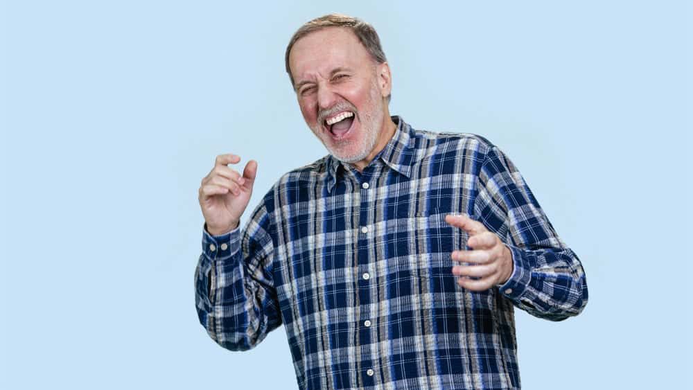 Happy mature man is laughing hard out loud. Isolated on pastel blue.