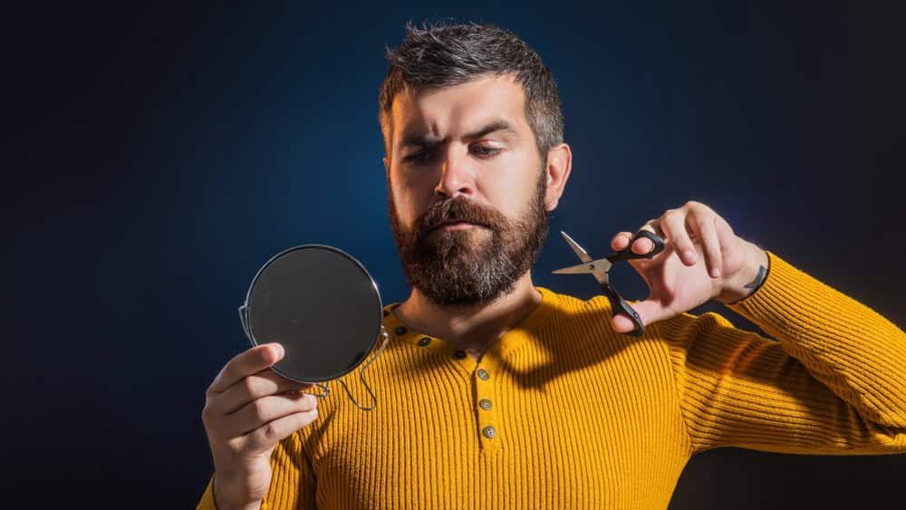 Barber scissors and mirror, barber shop. Cutting mustache and beard with barbers scissors. Bearded man without shaving. Man beauty. Take pride in your beard care routine. Beard care.