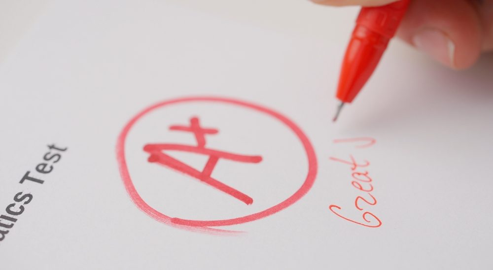 Professional school or college teacher grades a homework exam papers of students. Woman grades test with A plus and writes great job as comment.