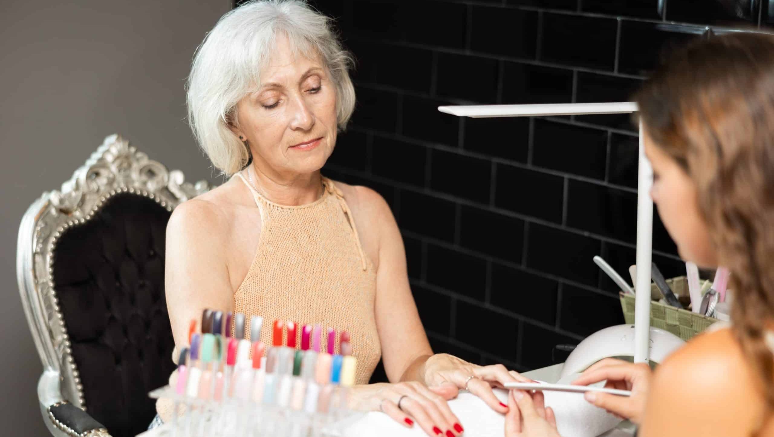 Smiling,Carefree,Elderly,Woman,Receiving,Manicure,From,Young,Female,Professional
