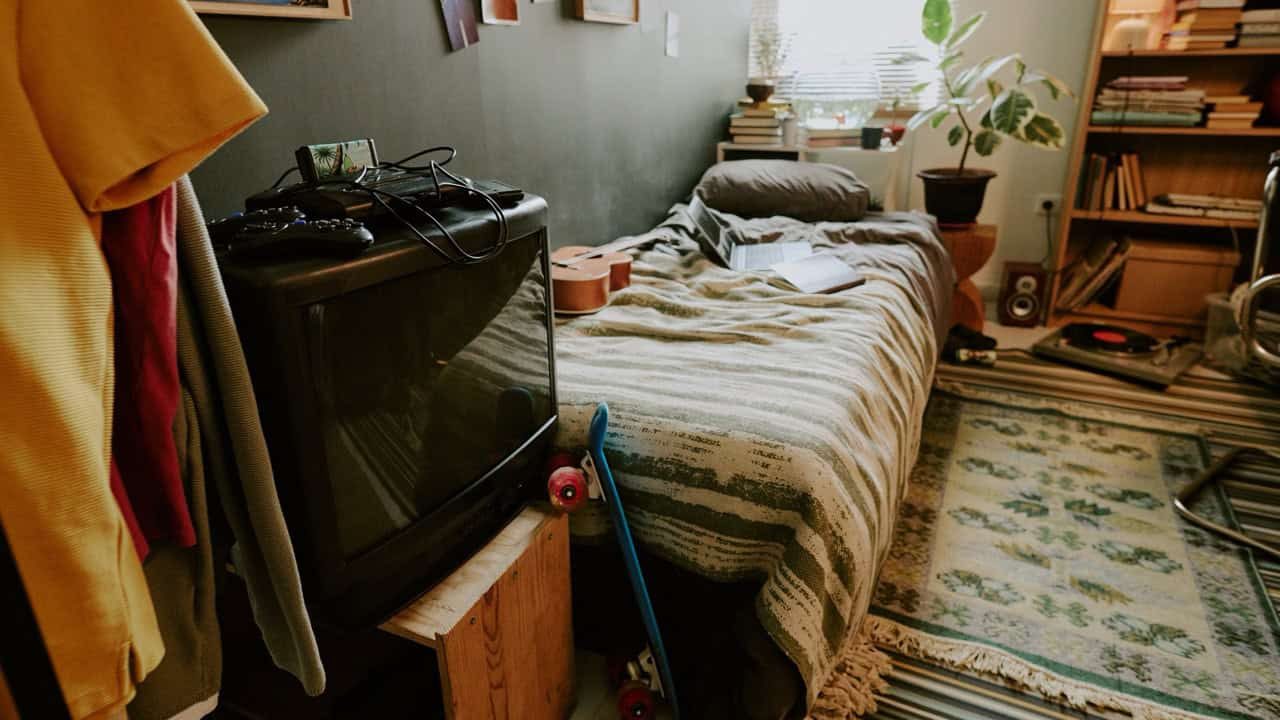 High angle shot of old fashioned TV on wooden nightstand next to single bed in cozy dormitory room