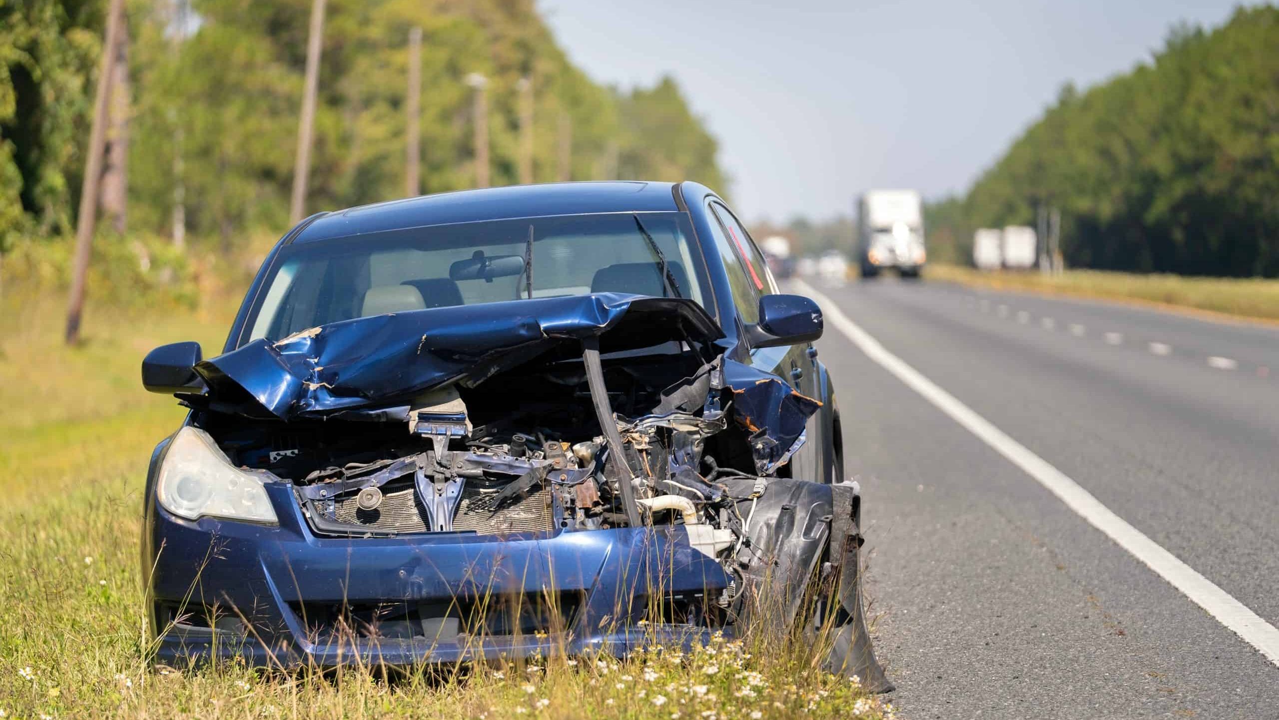 Old crashed car abandoned on highway road shoulder. Damaged in traffic accident vehicle parked on roadside