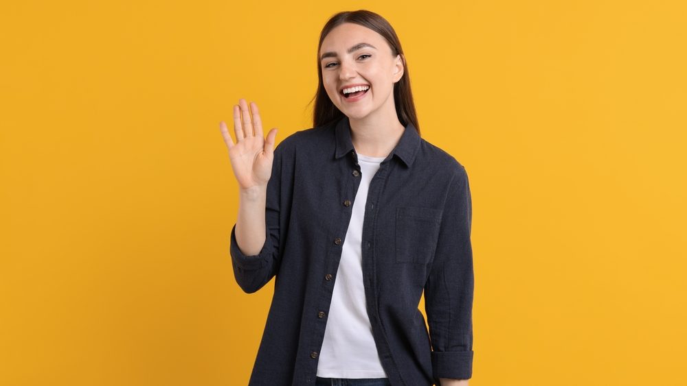 Happy young woman waving on orange background