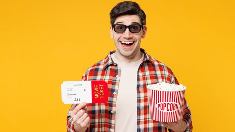 Young surprised happy man he wearing red checkered shirt casual clothes 3d glasses watch movie film hold ticket bucket of popcorn in cinema isolated on plain yellow orange background studio portrait