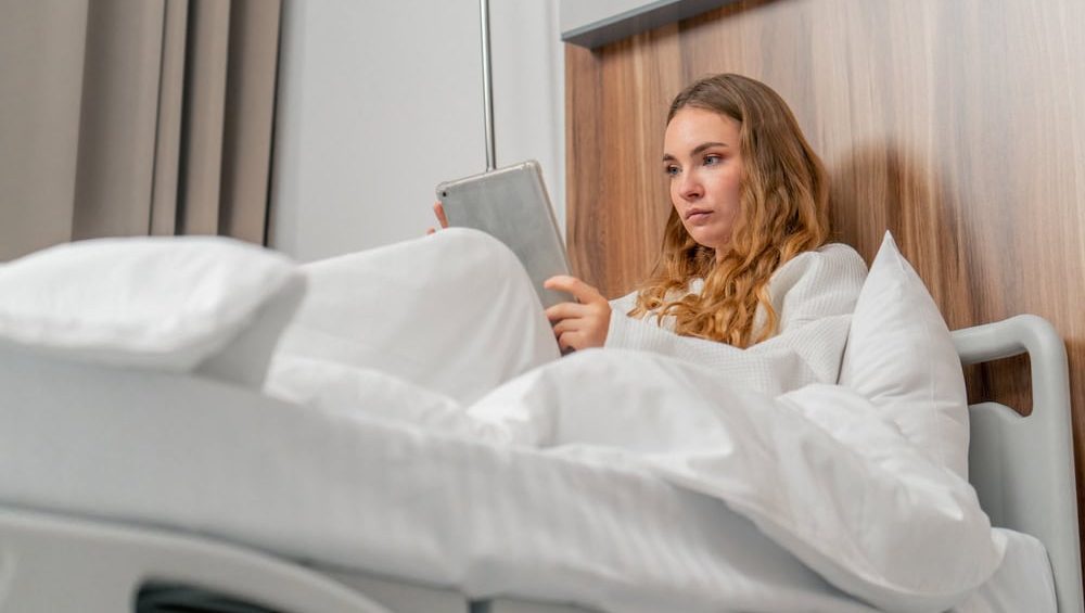 in modern clinic in a bright VIP room, a young girl in a white coat lies on a bed before an operation, flips through a tablet, looks at the options