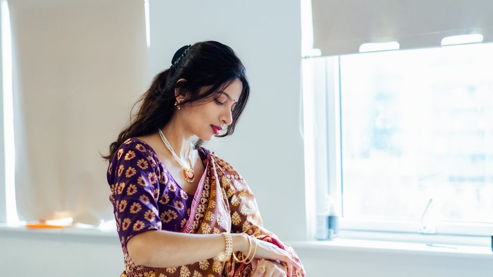 Dressed in beautiful saree, Indian woman delicately putting traditional jewellery getting ready for an ethnic festive celebration. Indian culture and ritual holidays in modern life. Selective focus.