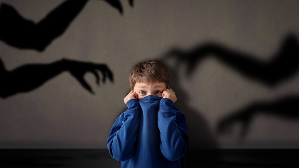 Little child scared by monstrous hands reaching for him. Shadows on grey wall