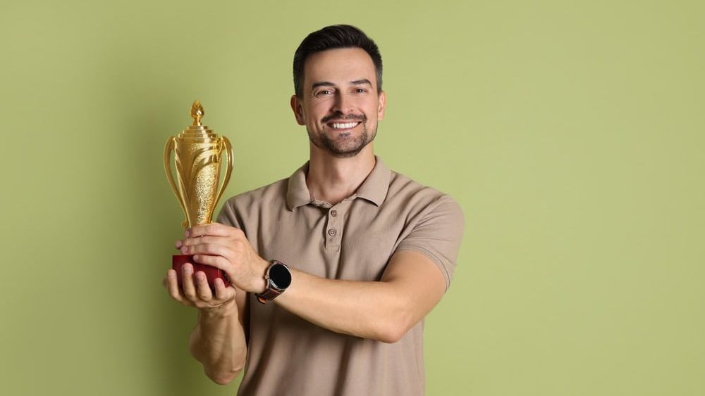 Happy winner with golden trophy cup on pale olive background
