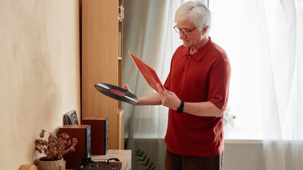 Side view portrait of white haired senior man holding vinyl records and choosing quiet home entertainment for relaxing evening copy space
