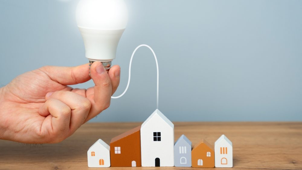 Hand connects light bulb to residential buildings. Concept of power supply. Innovations and technologies of smart home. Autonomous energy and housing. Energy saving.