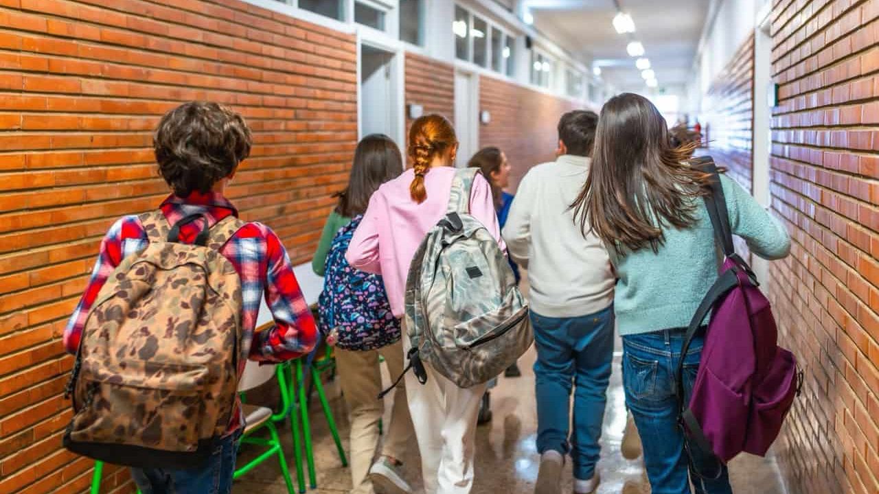 Group of students walking down school hallway between classes, carrying backpacks and rushing to their next lesson