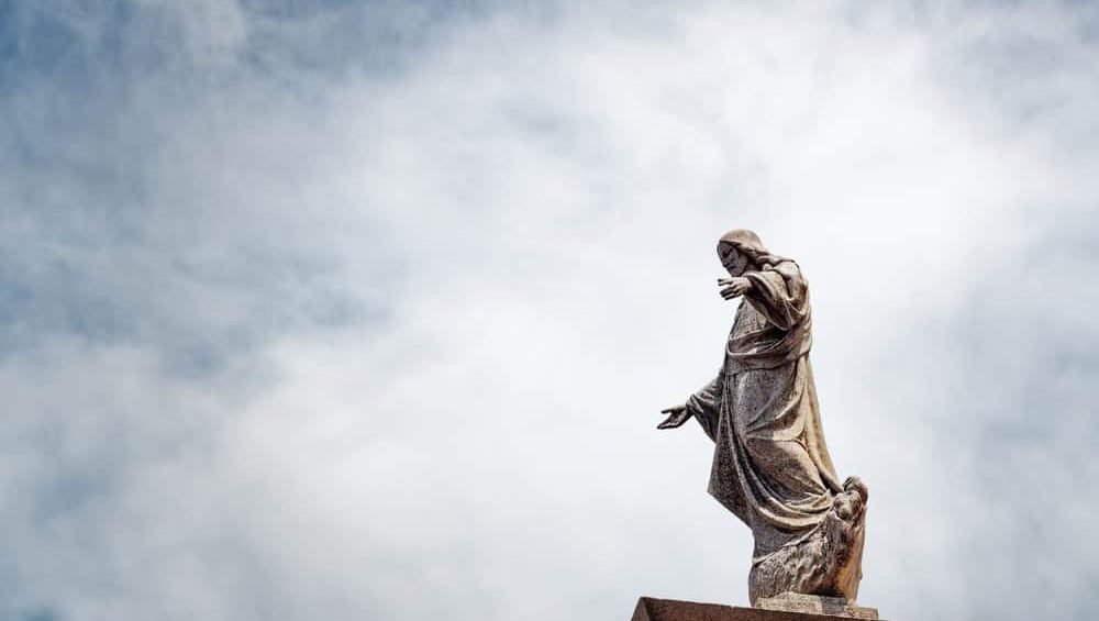 AYLLON, ES - Jul 14, 2020: Religious photography from a low angle, statue of Jesus Christ on a tower against a cloudy sky, capturing a serene and historical ambiance.