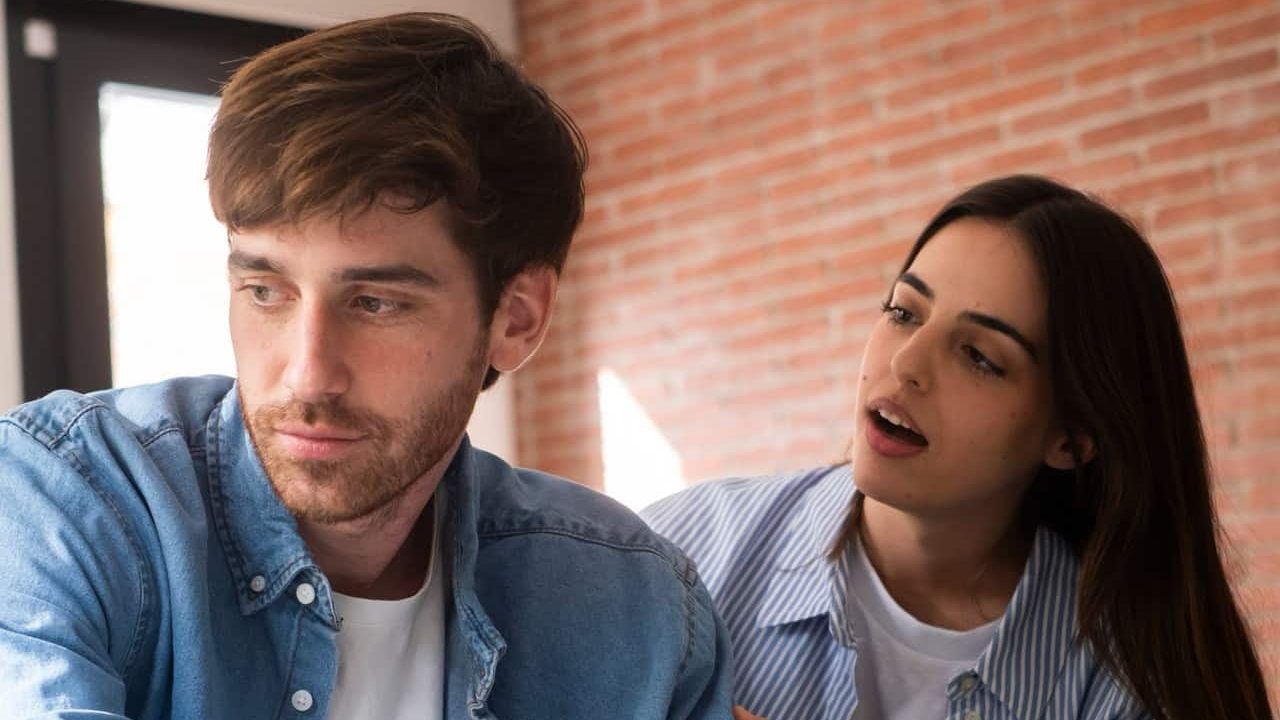 Unhappy man and woman sitting back-to-back on a sofa at home, facing emotional struggles due to trust issues, betrayal, relationship breakdown, and discussing their future while dealing with financial