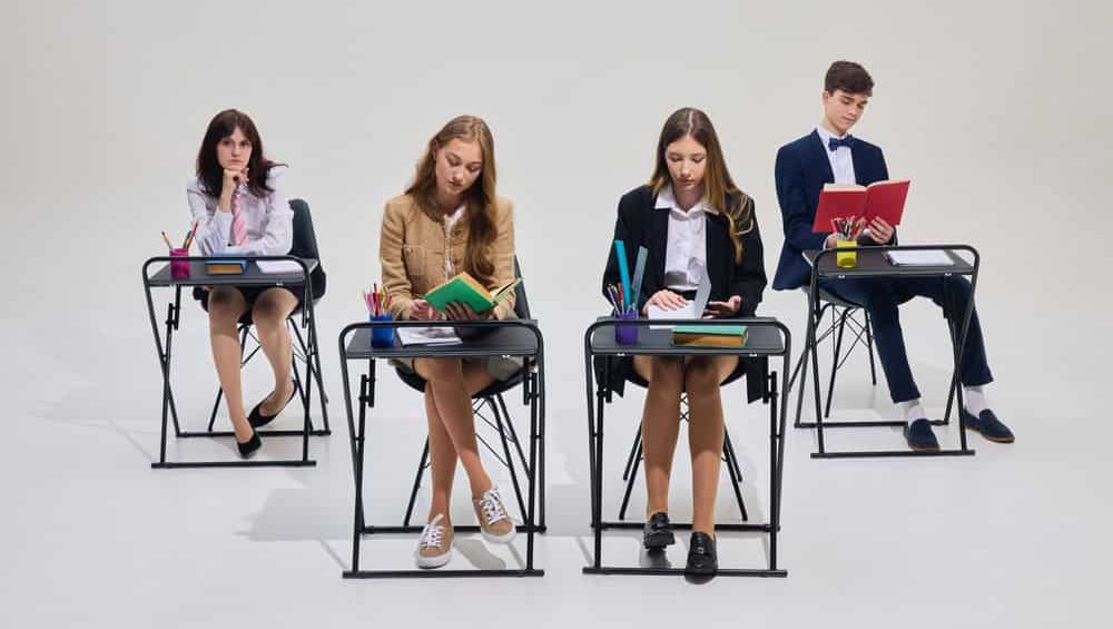 Group of high school students seating at desks reading and writing during quiet study session again studio background. Concept of student focus, classroom learning, school discipline.