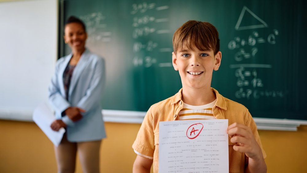 Happy schoolboy getting A+ grade on a test at elementary school and looking at camera.