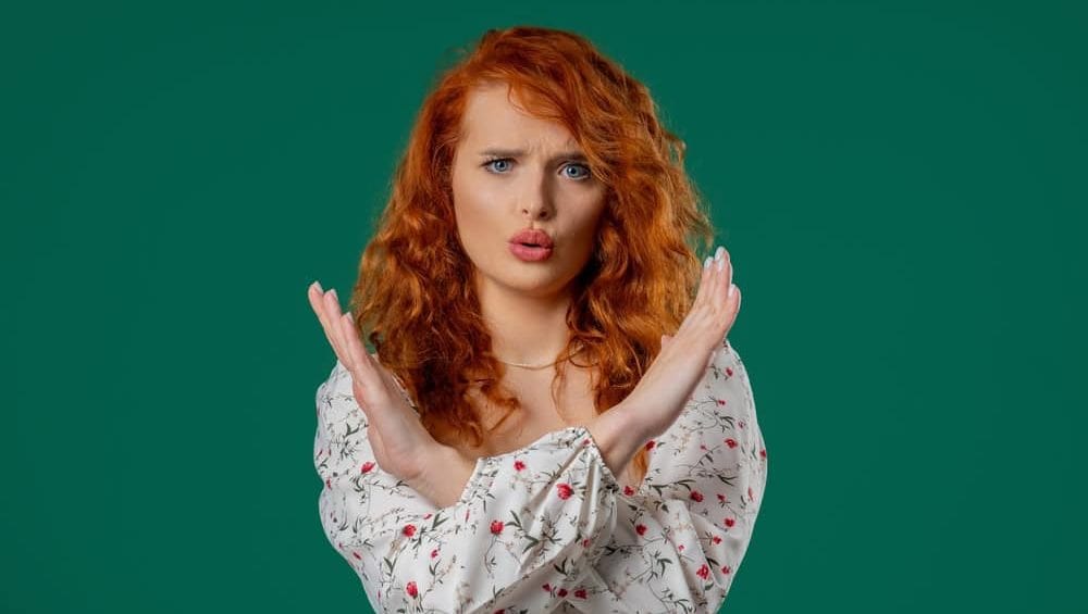 Assertive woman making stop gesture. Strong redhead lady showing hold sign