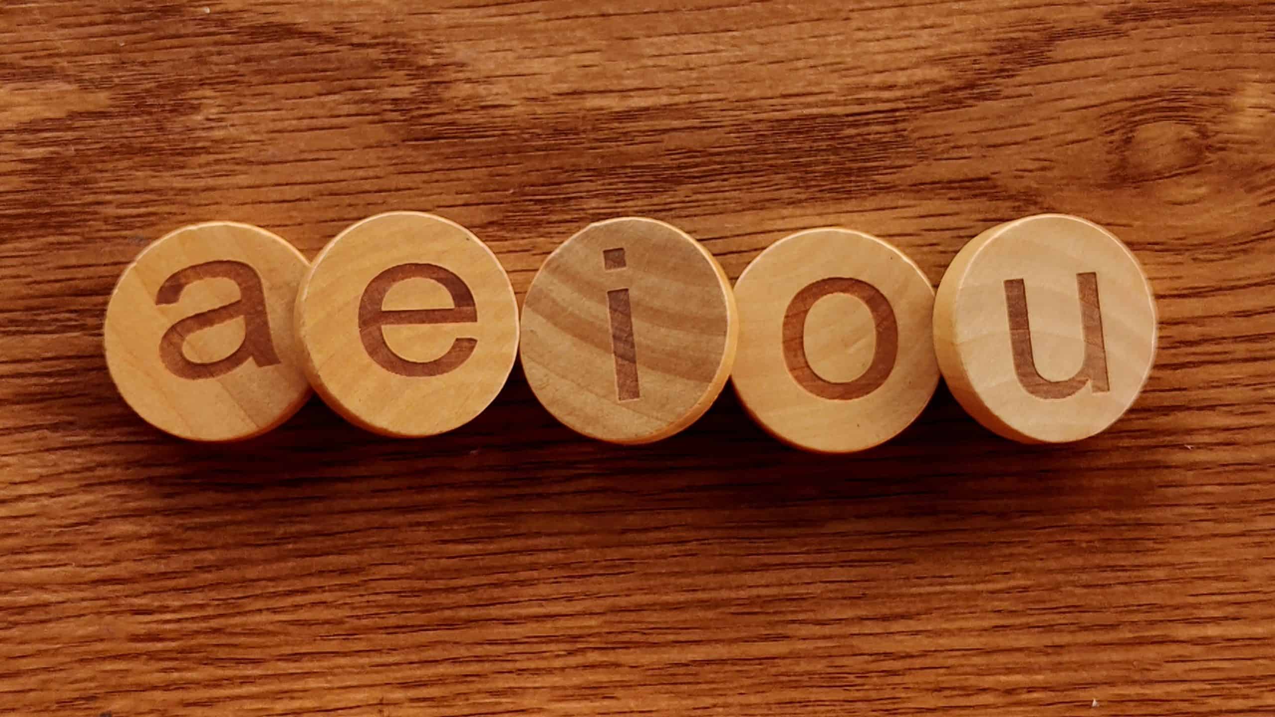 The Five Vowels: A-E-I-O-U Wooden Letters on a Natural Wood Background