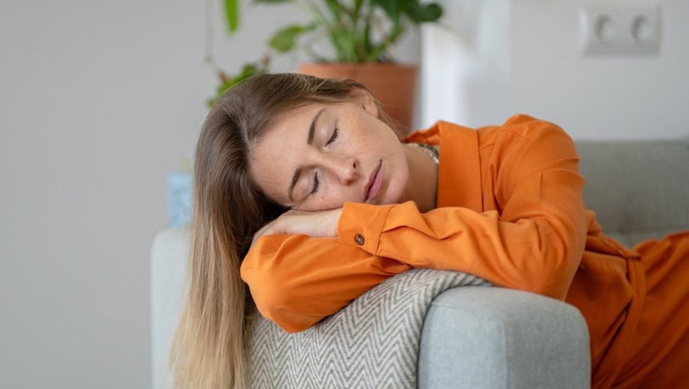 Serene middle-aged woman napping on sofa in ultimate calm, relaxation and silence. Female peaceful expression highlighting profound need and benefit of spontaneous rest, quiet reprieve from daily life