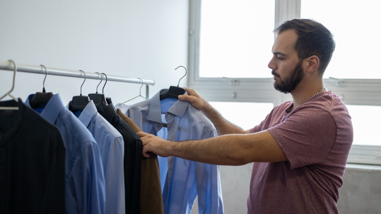 Man selecting a shirt from a rack while organizing his wardrobe