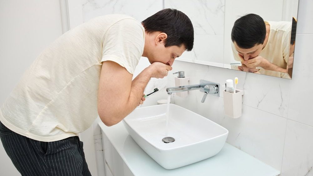 Man rinsing after brushing teeth over sink in modern bathroom