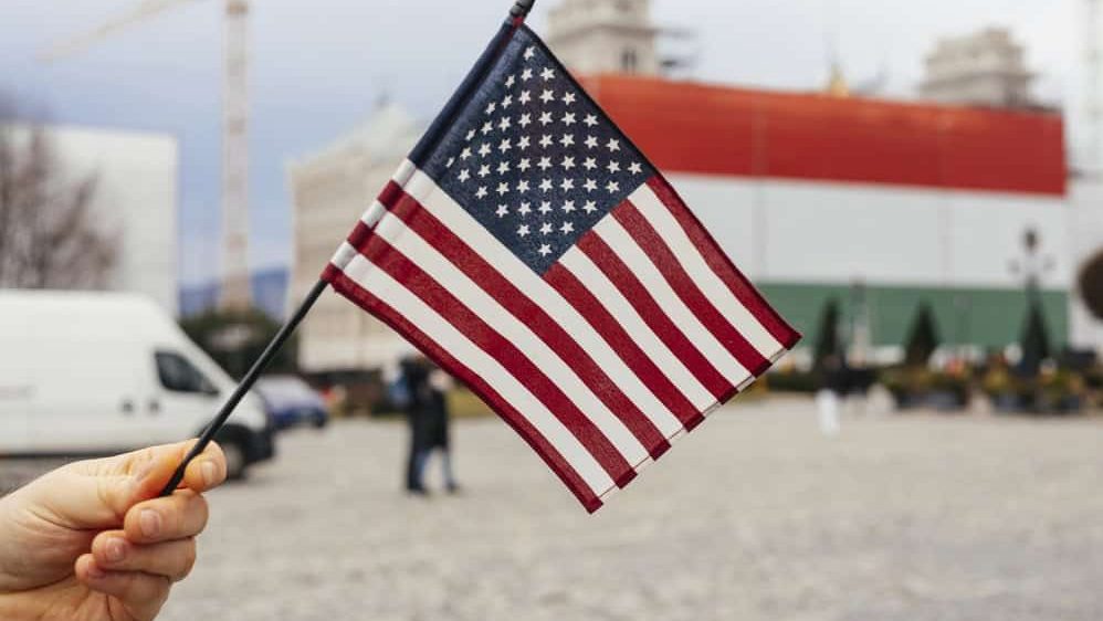 Hand holding USA flag over hungarian flag in Budapest, Hungary.