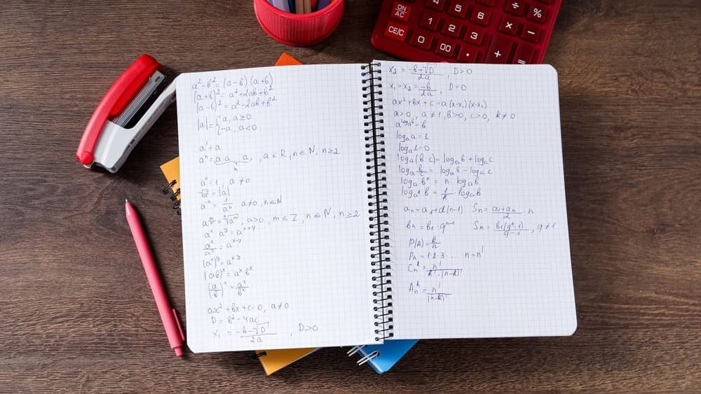Homework. Notebook with math formulas and different stationery on wooden table, flat lay