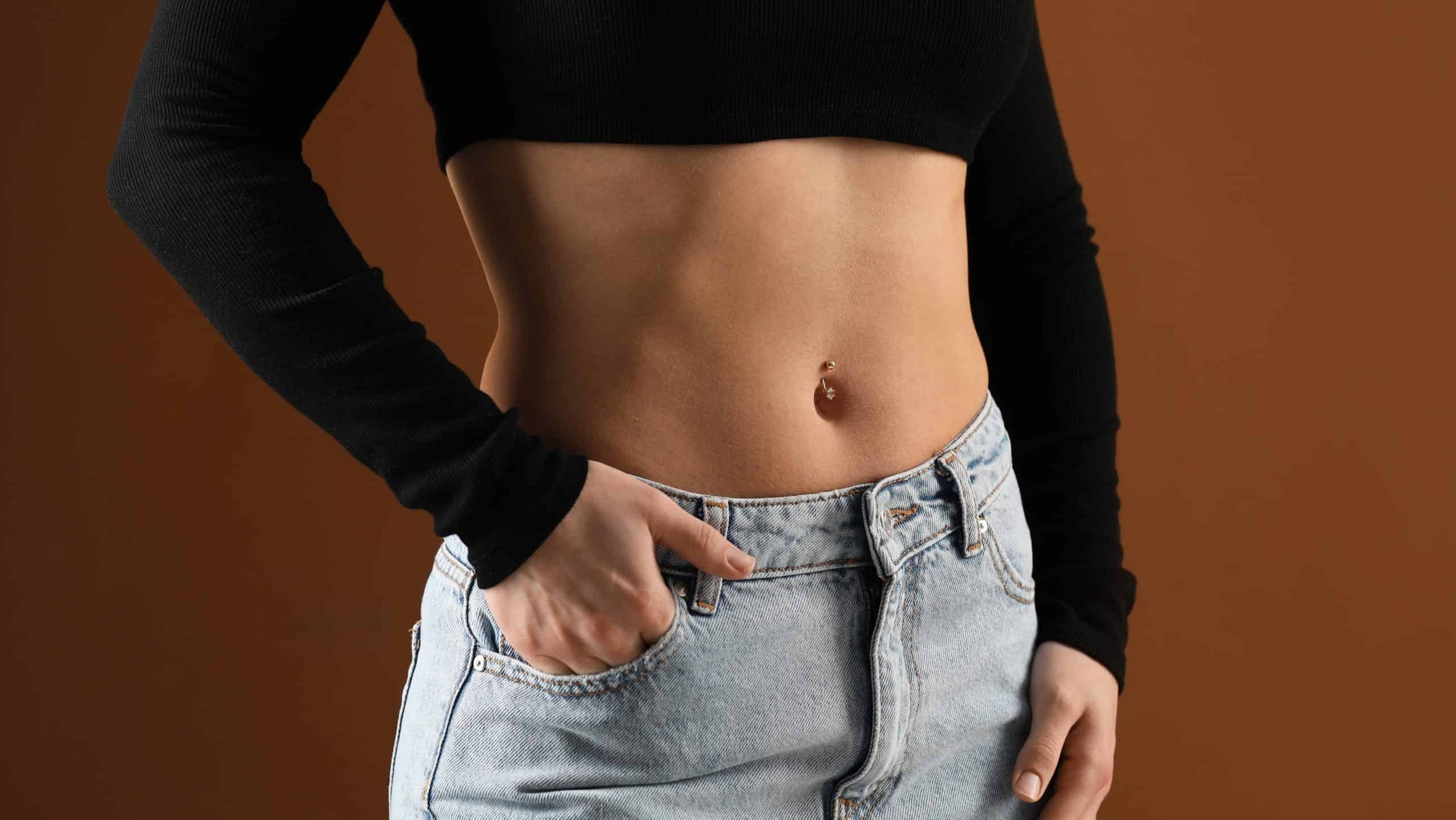 Woman with belly button piercing on brown background, closeup