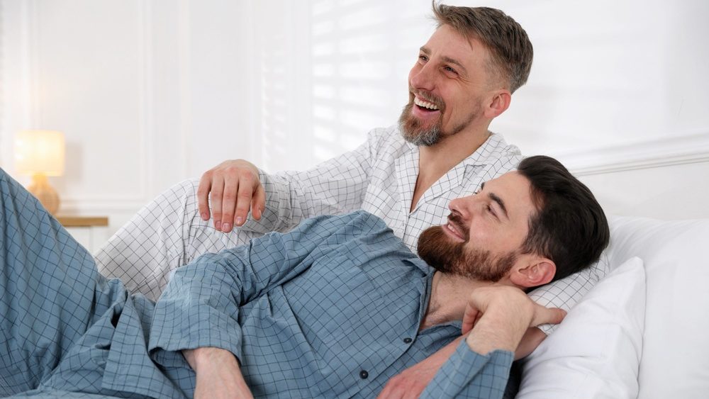 Happy gay couple together on bed at home