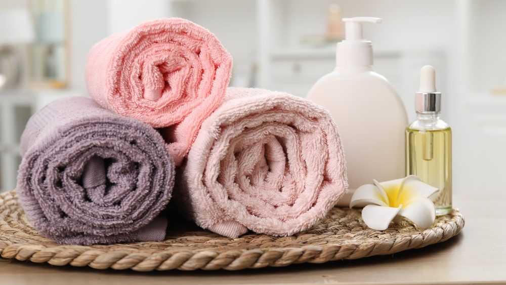 Colorful towels, cosmetic products and plumeria flower on wooden table indoors, closeup