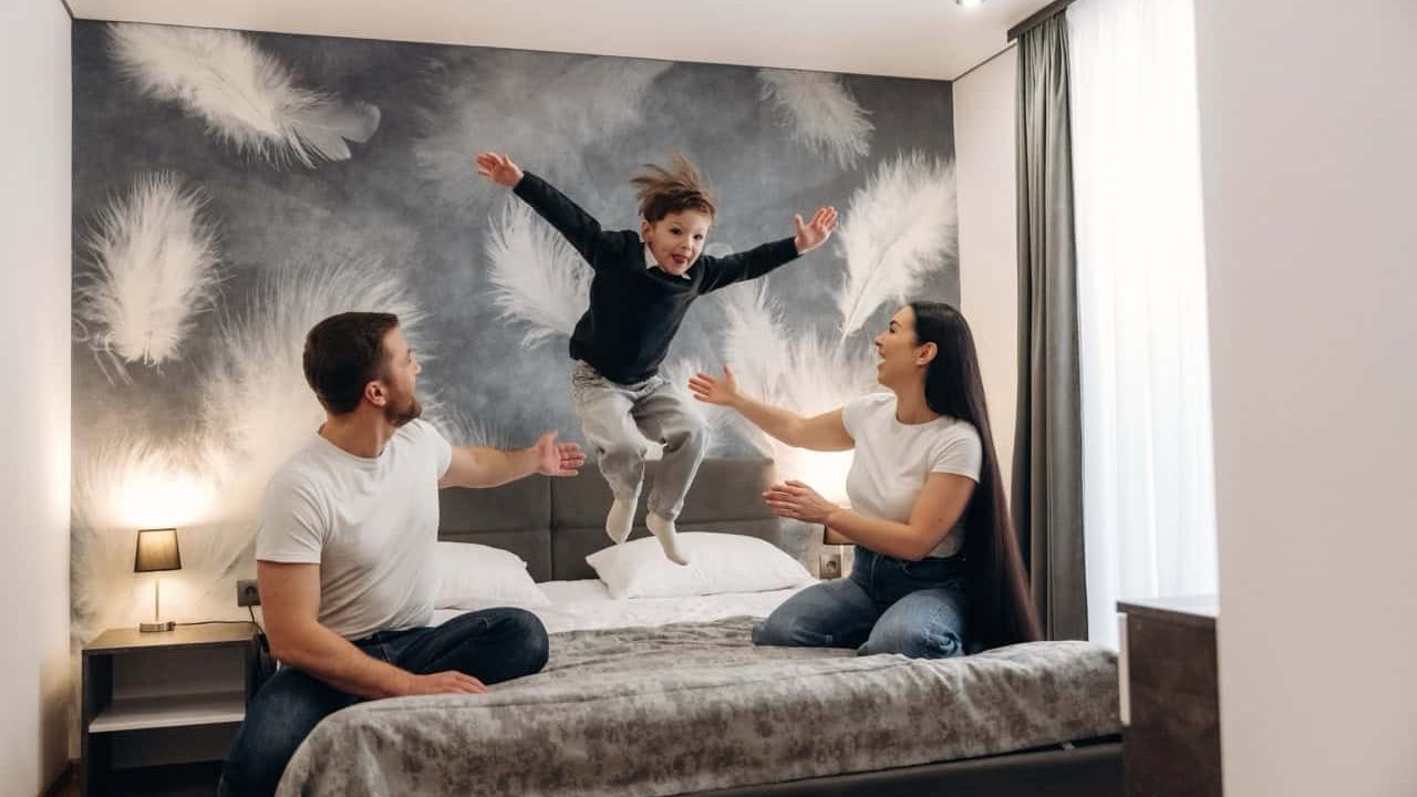 Family engages in playful activities in a contemporary hotel room featuring a feather-patterned wall and a cozy bed, enhancing their stay experience