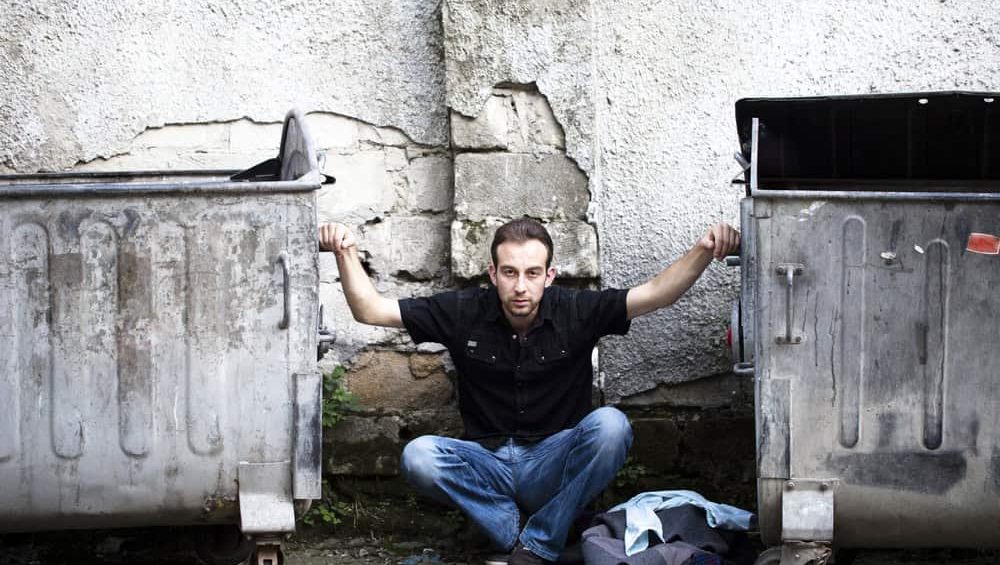 Person and city. A man is sat between two dustbins.