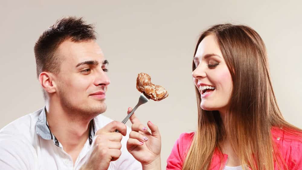 Smiling man feeding happy woman with cake. Wife and husband eating caloric food.