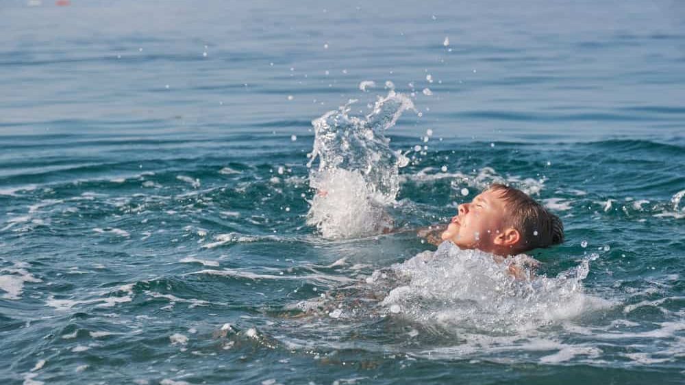 The child is drowning in the sea, screaming and waving his arms.